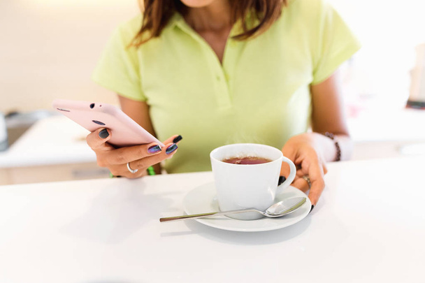 young household and business woman in the kitchen with smartphone and cup of tea - Foto, Bild