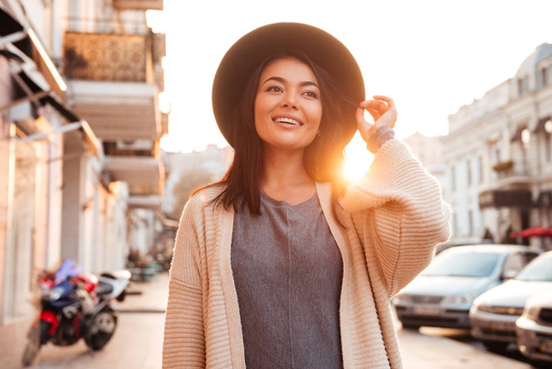 Happy attractive asian trendy woman adjusting her hat while walk - Foto, Imagem