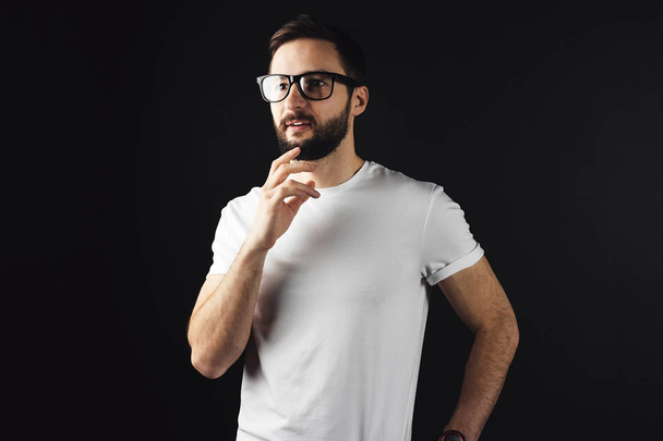 Pensive handsome man wearing in white blank tshirt on dark background. Bearded hipster posing in an empty t-shirt - Zdjęcie, obraz