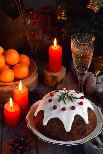 Traditioneller englischer Weihnachtspudding mit Winterbeeren, Trockenfrüchten, Nuss im festlichen Rahmen mit Weihnachtsbaum, brennender Kerze, Mandarinen und einem Glas Weißwein, Champagner. Obstkuchen. - Foto, Bild