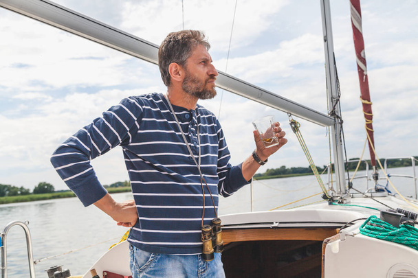 man with beard drinks whiskey on yacht - Valokuva, kuva
