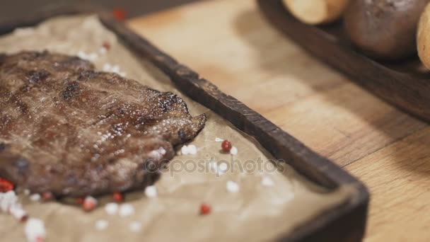 Kuchař je dokončení porce hovězí steak s pepřem, rozmarýnem a solí na dřevěné desce. Detailní záběr - Záběry, video