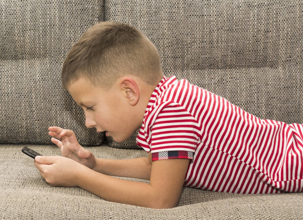 Pré-adolescent jouant avec un smartphone posé sur un canapé
 - Photo, image