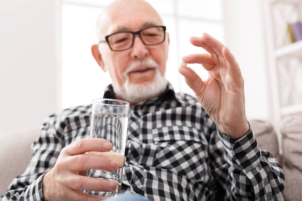 Vanha mies ottaa lasillisen vettä ja pillereitä kädessä
 - Valokuva, kuva