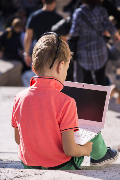 boy looks at a laptop on the steps and a lot of people - Foto, imagen