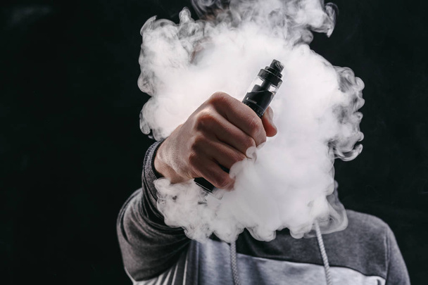 Junger Mann verdampft E-Zigarette mit Rauch auf schwarz - Foto, Bild