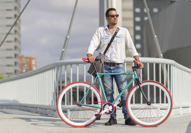 A young stylish man with sunglasses posing next to his bicycle. - Valokuva, kuva