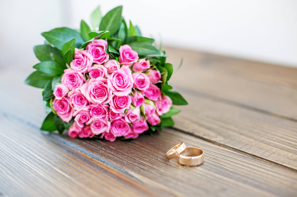 Wedding bouquet of pink roses and wedding rings on a wooden tabl - Photo, Image