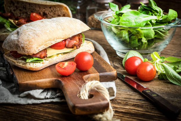 Ciabatta sandwich with arugula salad, bacon and yellow cheese. - Fotó, kép