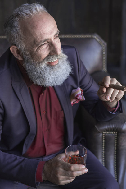 Smiling pensioner tasting alcohol and holding tobacco - Фото, зображення