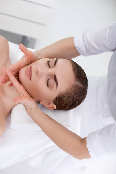 Skillful masseuse massaging female face at beauty salon - Foto, Imagem