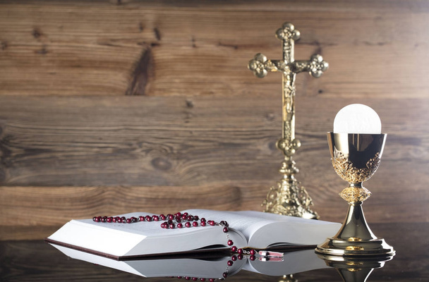 Katolikus vallás téma. A kereszt, Szent Biblia, Rózsafüzér és arany kehely, fából készült háttér. - Fotó, kép