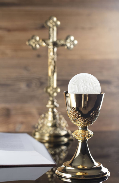 Catholic religion theme. The Cross, Holy Bible and golden chalice on wooden background. - Photo, Image