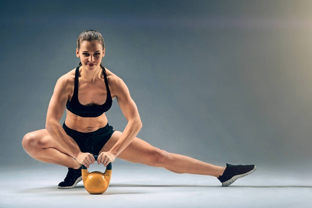 Friendly looking muscular girl posing with kettlebell - Foto, afbeelding