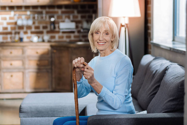 Cheerful pensioner sitting with a walking stick and smiling - Foto, imagen