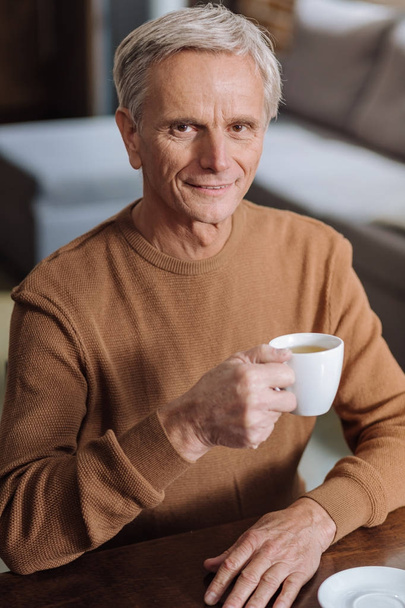 Cheerful calm senior man sitting with a cup of hot tea - Fotografie, Obrázek