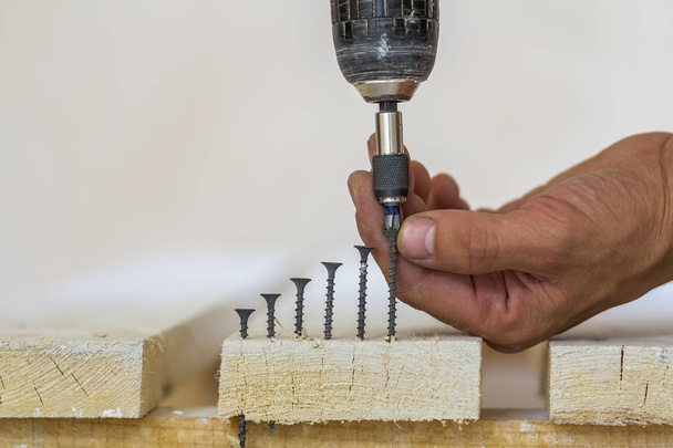 La mano del trabajador atornilla el tornillo en la tabla de madera con los cordones
 - Foto, Imagen