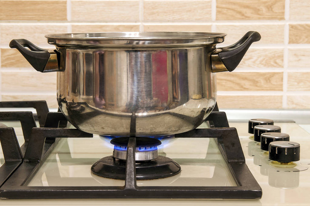 Metal cooking pot standing on kitchen stove with flame. - Foto, Imagen