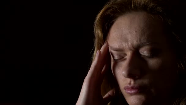 γκρο πλαν, λυπημένη γυναίκα με έναν πονοκέφαλο σε σκούρο φόντο. 4k, αργή κίνηση - Πλάνα, βίντεο