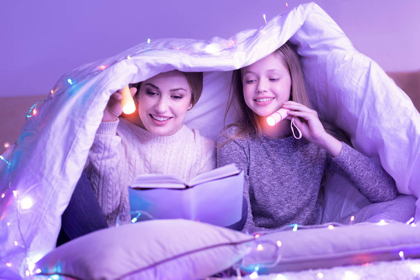 Devoted mom and daughter reading under the blanket - Фото, зображення