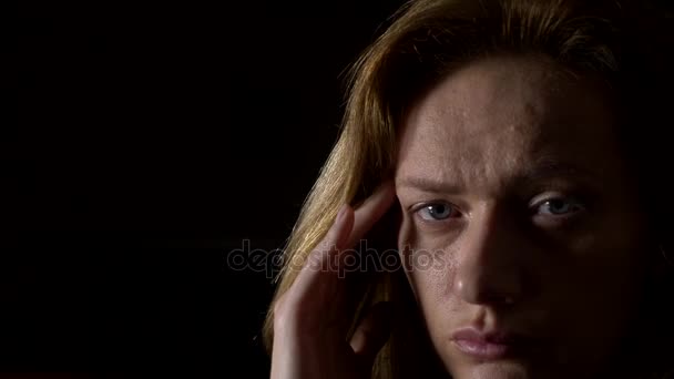 Close-up, trieste vrouw met een hoofdpijn op een donkere achtergrond. 4k, slow-motion - Video