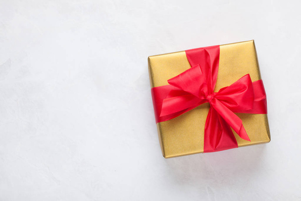 Caja de regalo dorada atada con una cinta roja aislada sobre fondo blanco. Vista superior. Copiar espacio
 - Foto, Imagen