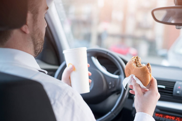 Homme mangeant un hamburger et conduisant assis en voiture
 - Photo, image