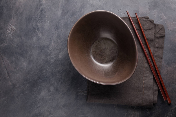 Empty glass bowl of Chinese noodles and wooden sticks on dark concrete background. Top view with copy space. Flat lay - Photo, Image