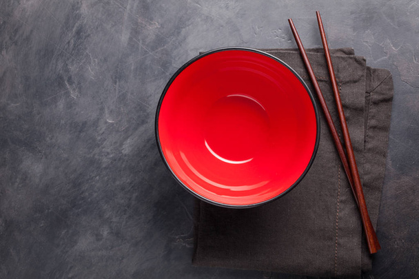 Empty red glass bowl of Chinese noodles and wooden sticks on dark concrete background. Top view with copy space. Flat lay - Foto, Imagem