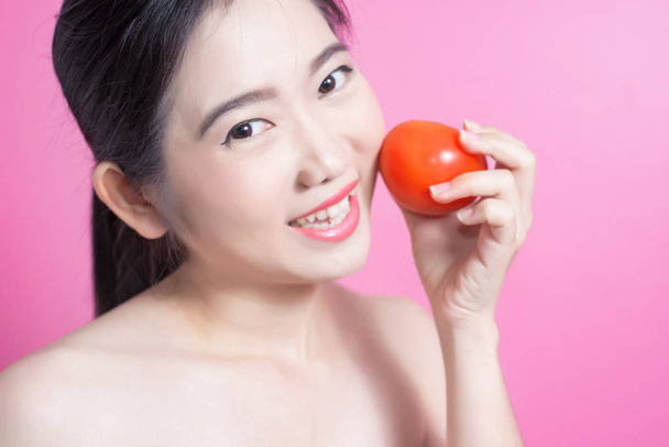 Asiatin mit Tomatenkonzept. sie lächelt und hält Tomate in der Hand. Schönheit Gesicht und natürliches Make-up. isoliert über rosa Hintergrund. - Foto, Bild