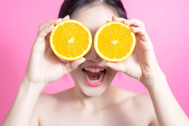 Ázsiai nő narancssárga koncepció. Ő mosolyogva, és a gazdaság narancs. Kozmetikai arc és a természetes smink. Elszigetelt, felett rózsaszín háttér. - Fotó, kép