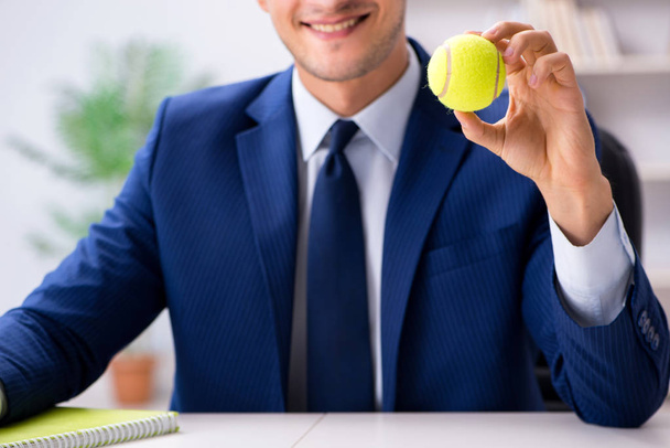 オフィスで働いているテニスボールを持つ若いビジネスマン - 写真・画像