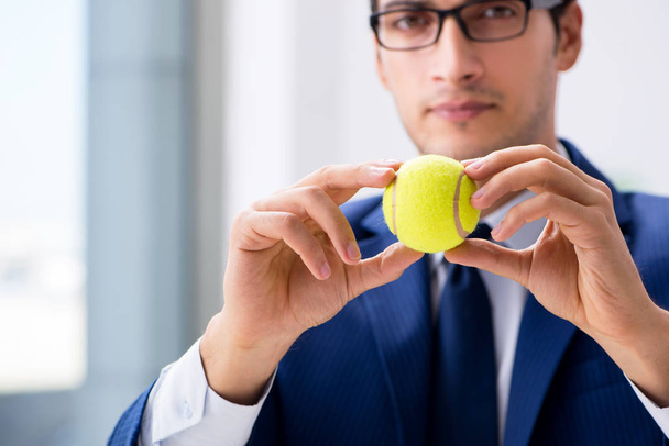 Young businessman with tennis ball working in office - Foto, imagen