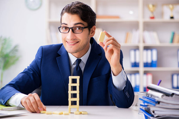 Молодой бизнесмен строит домино башню в офисе - Фото, изображение