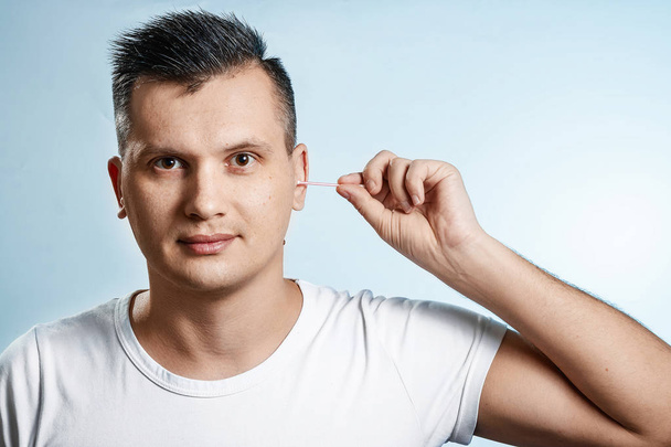 The man with the help of a hygienic cotton swab is reading his ear. The concept of body hygiene. - Valokuva, kuva