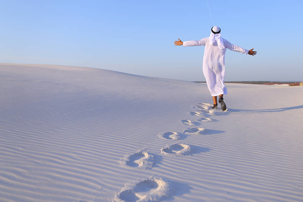 Alegre macho musulmán camina por el desierto de arena blanca y disfruta li
 - Foto, Imagen