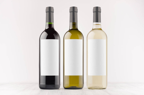 Transparent, green, black wine bottles with blank white labels on white wooden board, mock up. Template for advertising, design, branding identity. - Foto, Bild