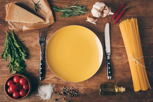 top view of row pasta, fresh ingredients and plate with knife and fork on wooden table - Photo, Image