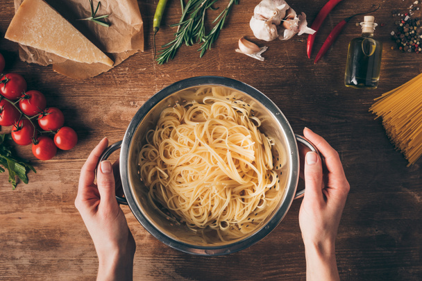 top view of hands with spaghetti pasta and ingredients on wooden tabletop - Foto, afbeelding