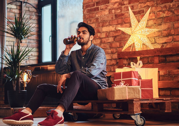 attraktive bärtige indische Männchen trinkt Craft Beer in einem Raum mit Weihnachtsdekoration. - Foto, Bild