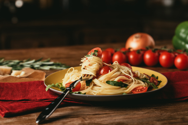 macarrão italiano tradicional com tomate e rúcula em prato com garfo
 - Foto, Imagem