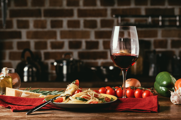 pasta italiana tradicional con tomates y rúcula en plato y copa de vino tinto
 - Foto, Imagen