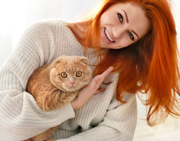 Hermosa joven con gato rojo. gato doméstico escocés Doblar primer plano
. - Foto, imagen