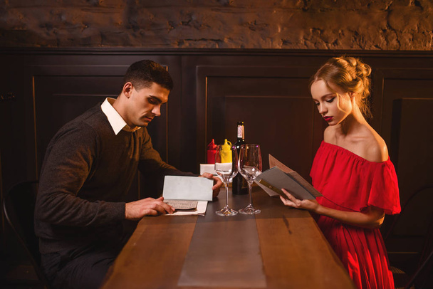 Giovane coppia d'amore al ristorante, appuntamento romantico. Elegante donna in abito rosso e bell'uomo guardando il menu
 - Foto, immagini