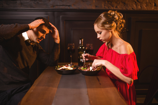 Quarrel of young couple in restaurant, bad romantic date. Elegant woman in red dress and handsome man dining  - Photo, Image