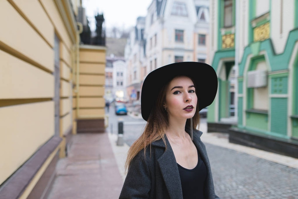 美しい古い町の通りの背景にスタイリッシュな女性のストリートの肖像。色の古い建築の背景に帽子の美しい少女が立っています。 - 写真・画像