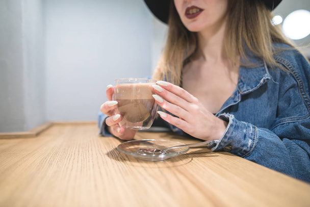 Una taza de café en la mano de una mujer con una hermosa manicura. La chica hipsters sostiene una taza de bebida caliente. Concéntrate en la copa
. - Foto, Imagen