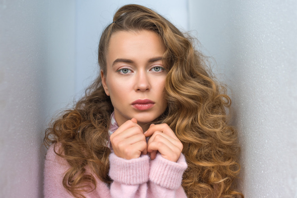 portrait of serious girl with long curly hair looking at camera and standing between walls - Foto, afbeelding