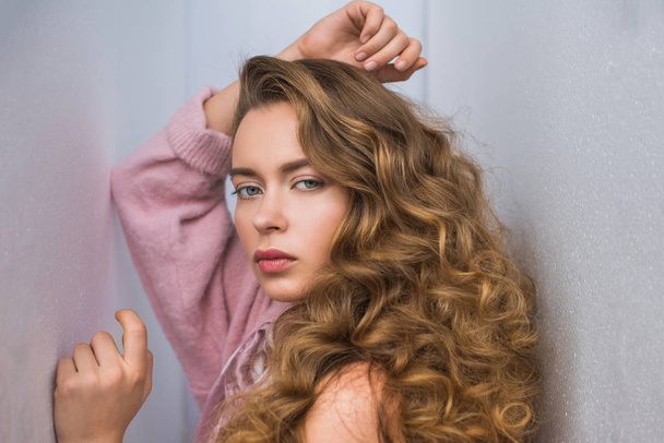 fashionable woman with curly hair posing for fashion shoot between gray walls - Photo, Image