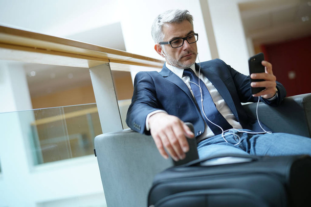 Businessman in airport waiting area connected with smartphone - Фото, изображение